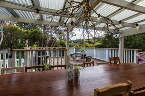 A wooden dining table with chairs, a hanging light fixture, and a view of the outdoors. - Hekerua Lodge Boutique Backpackers (Waiheke Island)