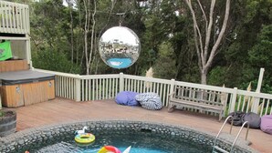 Una piscina con juguetes inflables de unicornio, una terraza de madera, una valla blanca y una gran bola de discoteca.