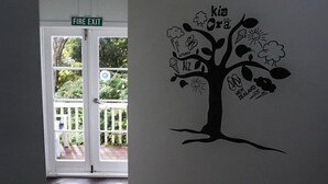 Un pasillo con un letrero de salida de incendios, un adhesivo de árbol con la frase 'Kia Ora' y 'Nueva Zelanda' en la pared, y piso de madera.