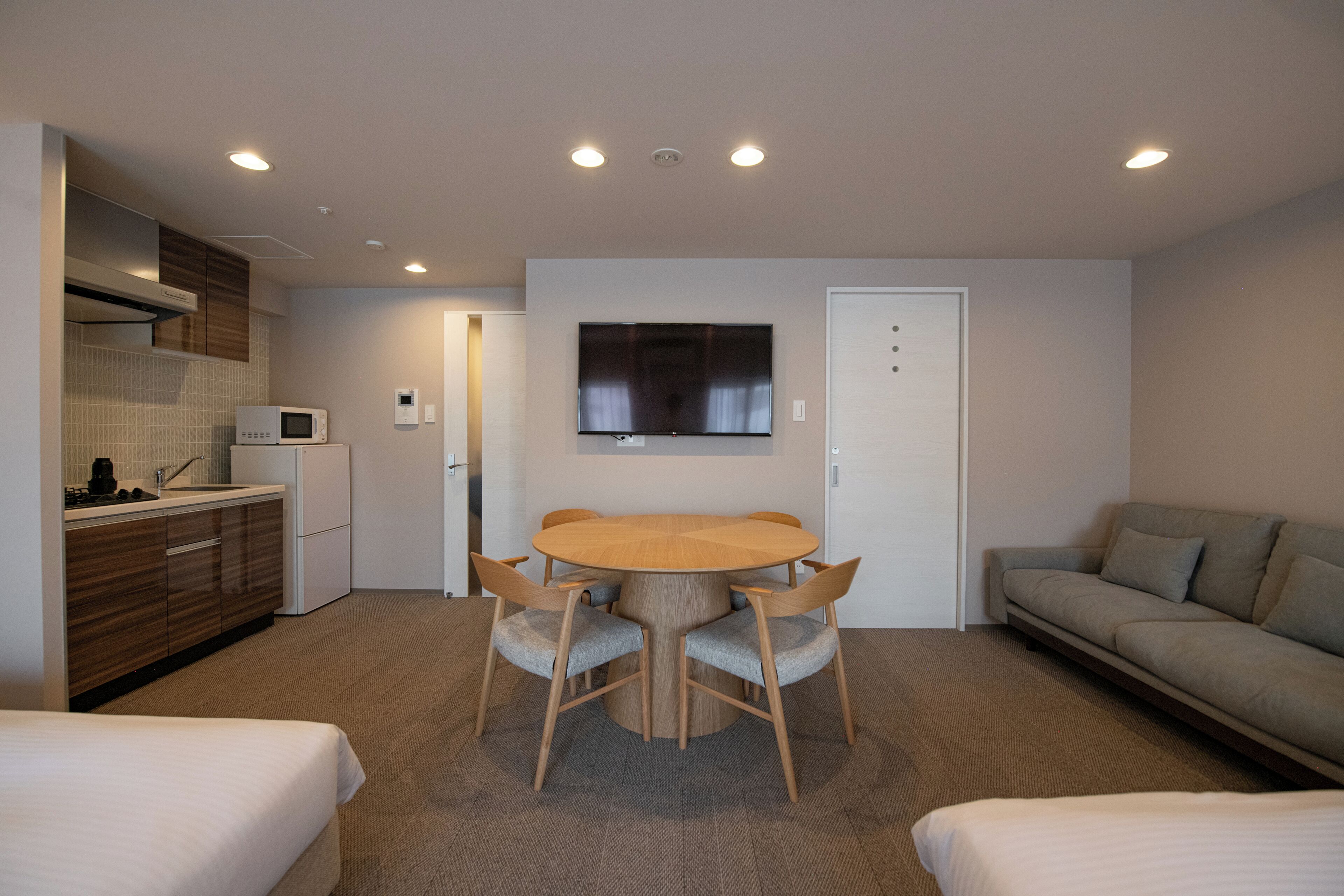 Habitación de hotel compacta con kitchenette, una mesa redonda con cuatro sillas, un televisor de pantalla plana en la pared, un sofá y dos camas.