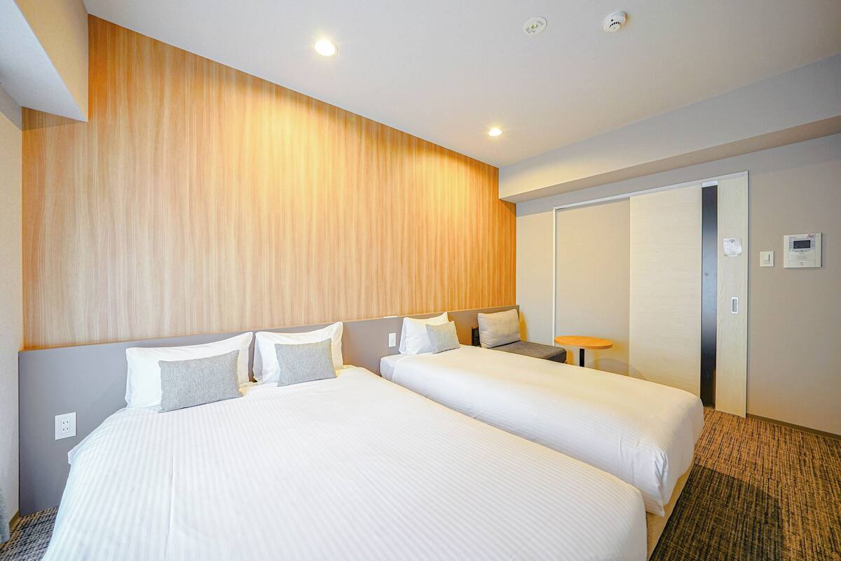 A hotel room with two beds, a wooden headboard, a small table, and a door with a mirror.