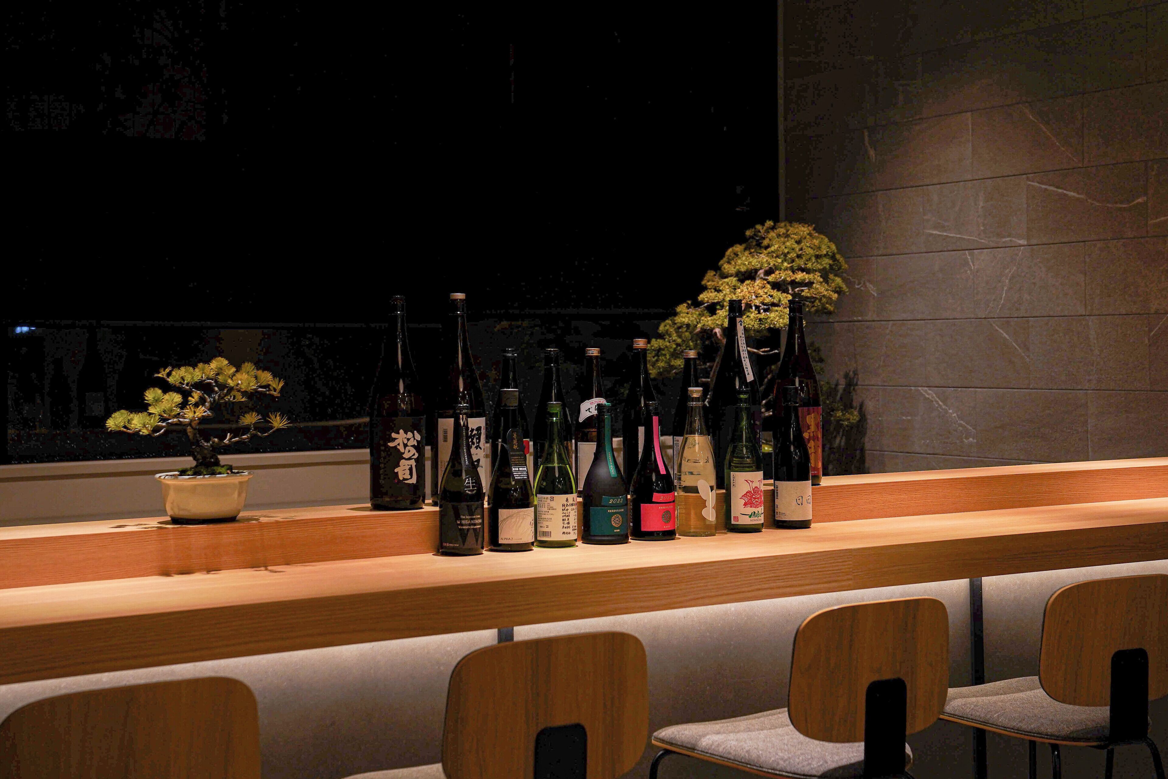 Zona de bar con mostrador de madera que exhibe diversas botellas de alcohol y una planta en maceta.