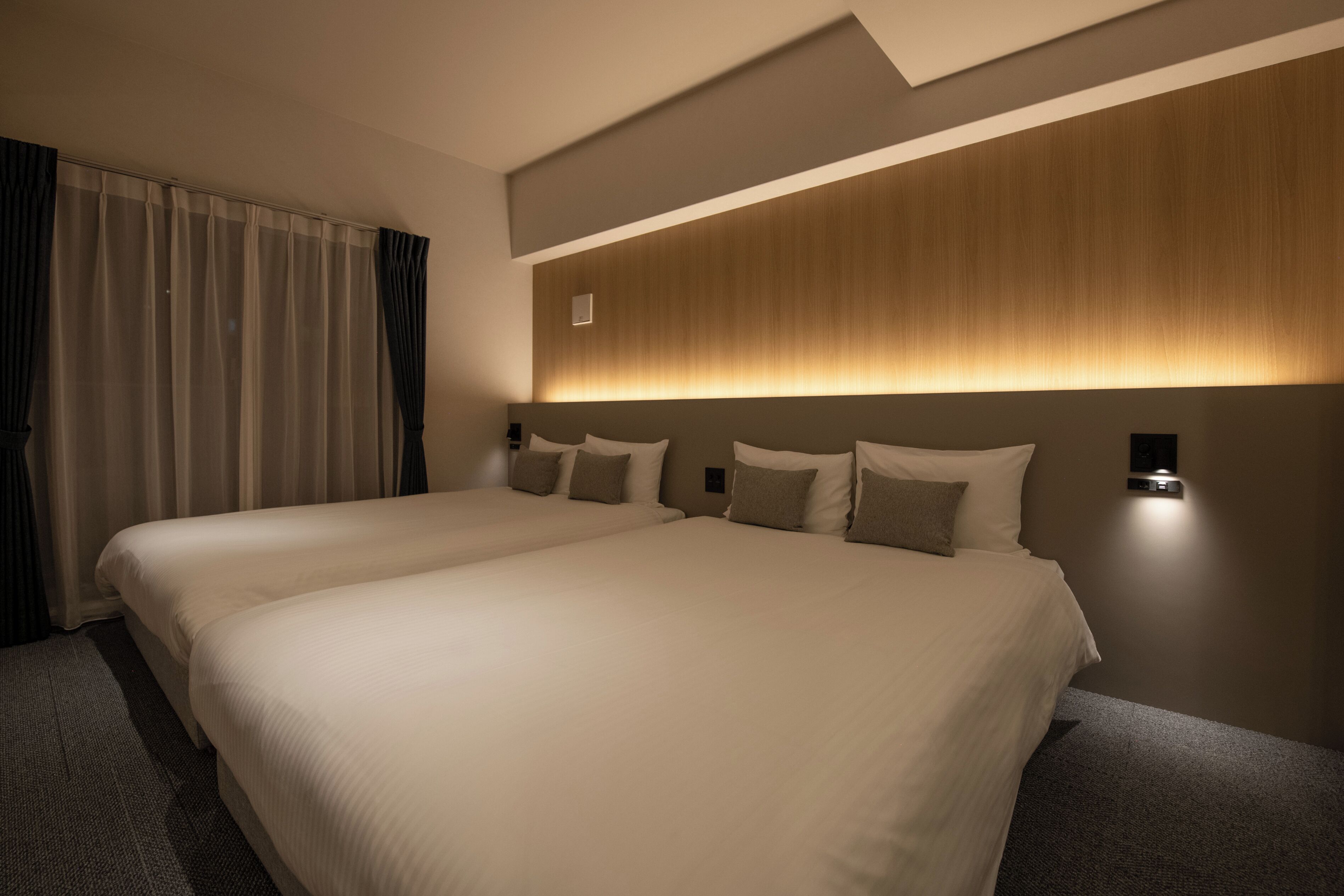 A hotel room with two large beds, a wooden headboard, and a wall-mounted light fixture.
