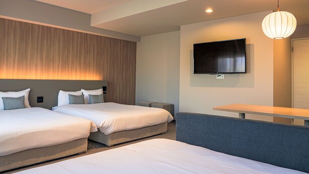 Ein Hotelzimmer mit zwei Betten, einem Fernseher, einem Sofa und einem Schreibtisch.