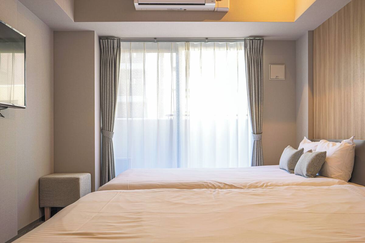 A hotel room with a large bed, a small bedside table, and a window with curtains.