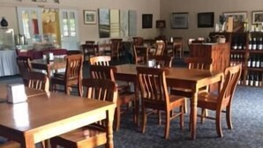A dining area with wooden tables and chairs, a patterned carpet, and framed pictures on the walls.