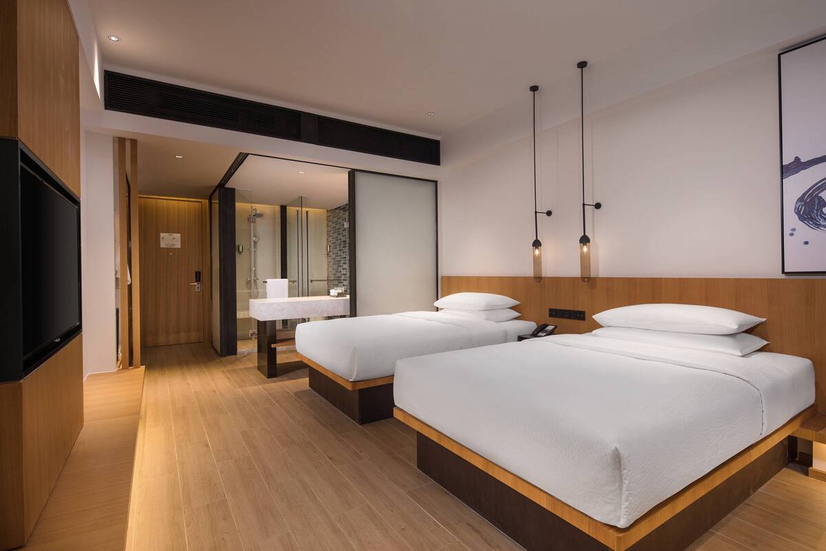A modern hotel room with two beds, a large mirror, a TV, and a wooden floor.