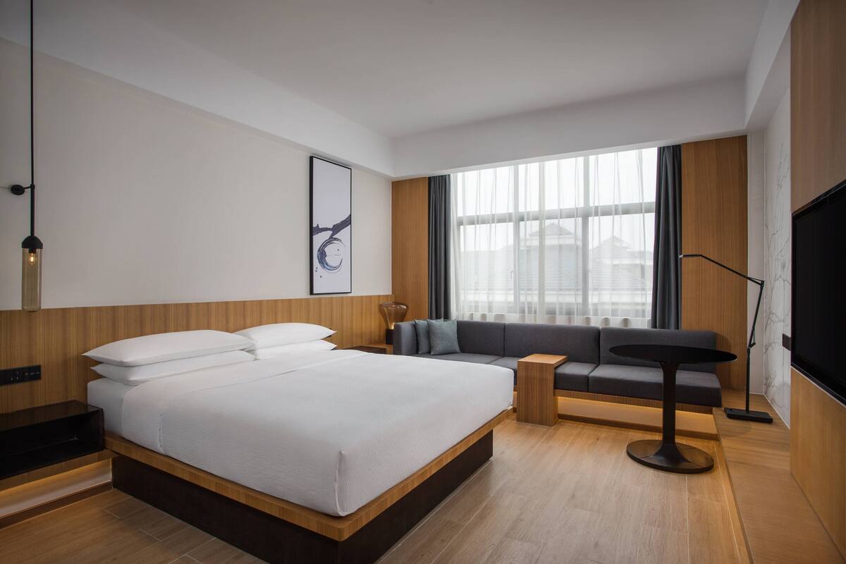 A modern hotel room with a large bed, a sofa, a small table, and a TV.