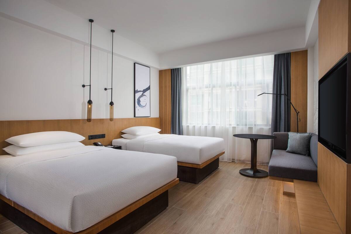 A hotel room with two beds, a sofa, a TV, and a small table.