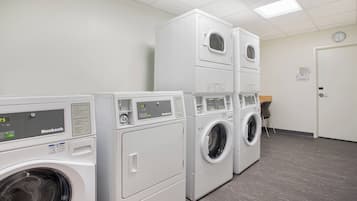 A laundry facility with multiple rows of white, front-loading washing machines and dryers.