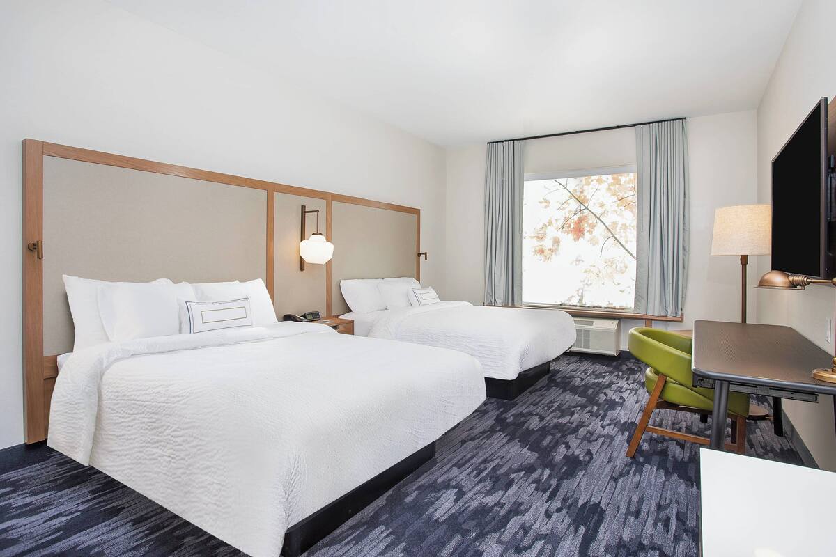 A hotel room with two beds, a desk, a chair, a TV, and a window with curtains.