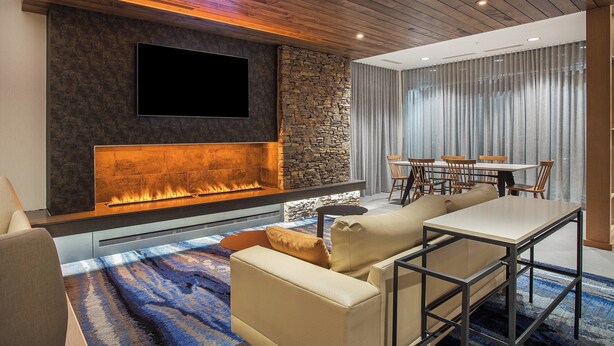 A modern living room with a stone fireplace, a flat-screen TV, and a dining area with a table and chairs. - Fairfield Inn & Suites by Marriott Pigeon Forge (Pigeon Forge)