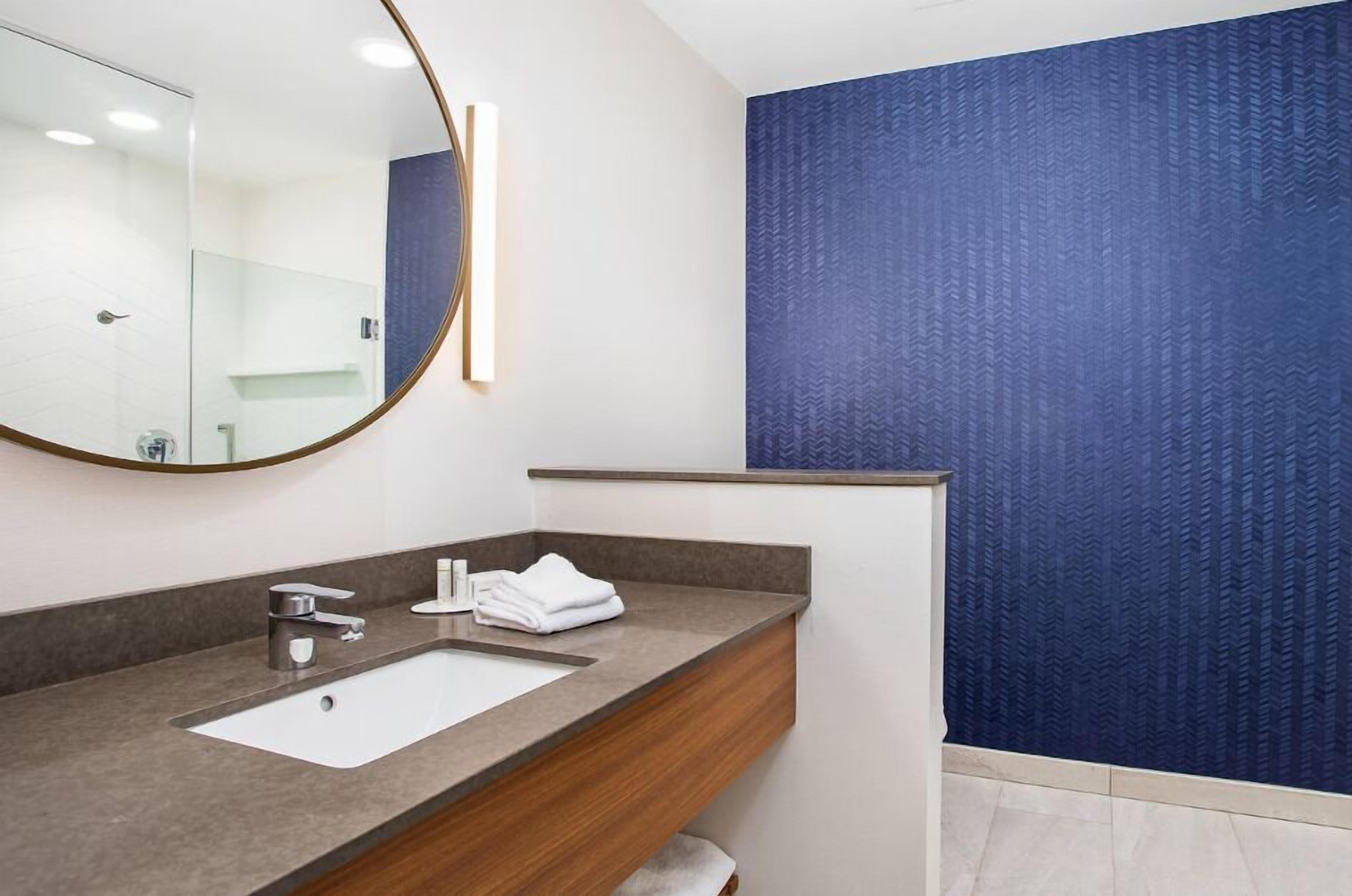 A modern bathroom with a large mirror, a sink, and a towel.
