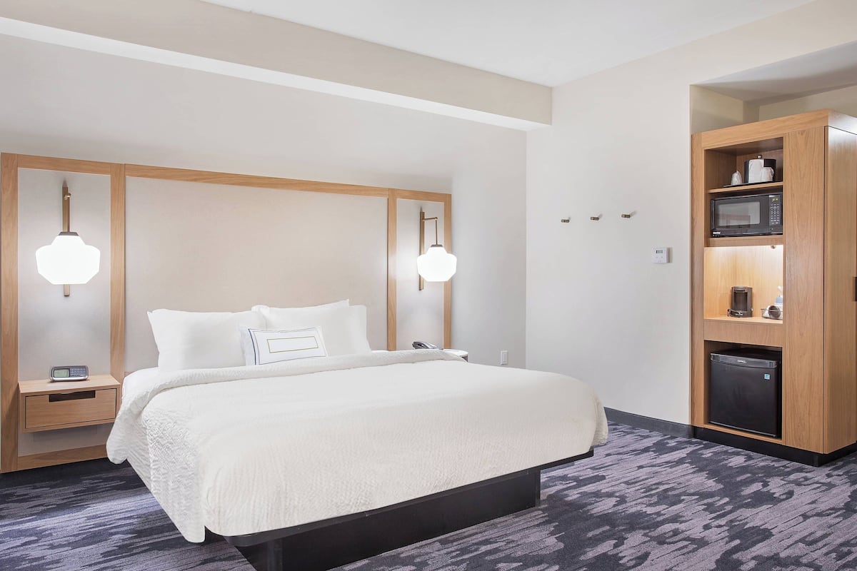 Une chambre d’hôtel avec un grand lit, des tables de chevet, un four à micro-ondes encastré et un petit réfrigérateur.