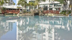 A pool with a bridge, palm trees, and a building in the background.