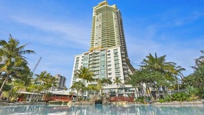 A tall hotel with a pool surrounded by palm trees.