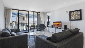 Een moderne woonkamer met een bank, een salontafel en een televisie. Er is een balkon met uitzicht op gebouwen.