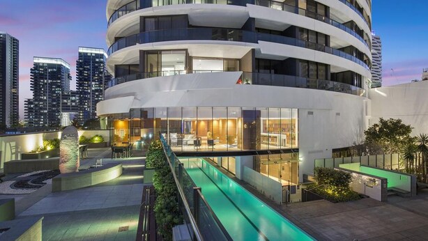 Een modern hotel met een gebogen gevel, buitenzwembad en weelderige beplanting.