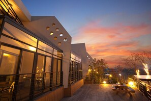 A modern building with large windows and a wooden deck with tables and chairs. - Healing 11st Pension (Incheon)