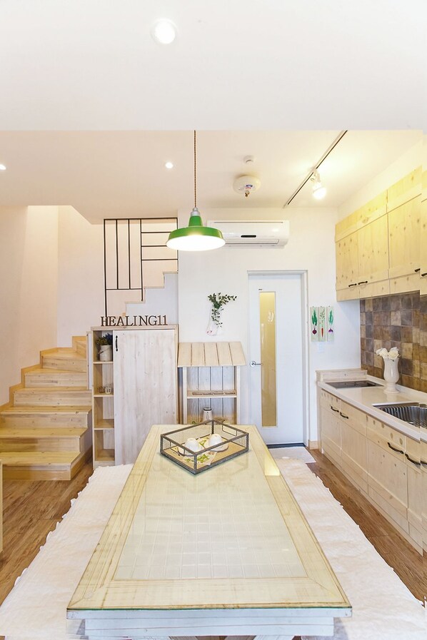 A modern kitchen with wooden cabinets, a central island, and a staircase with a 'HEALING' sign. - Healing 11st Pension (Incheon)