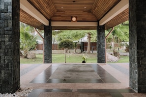 A covered outdoor area with a stone wall, a wooden ceiling, and a view of a fenced garden.