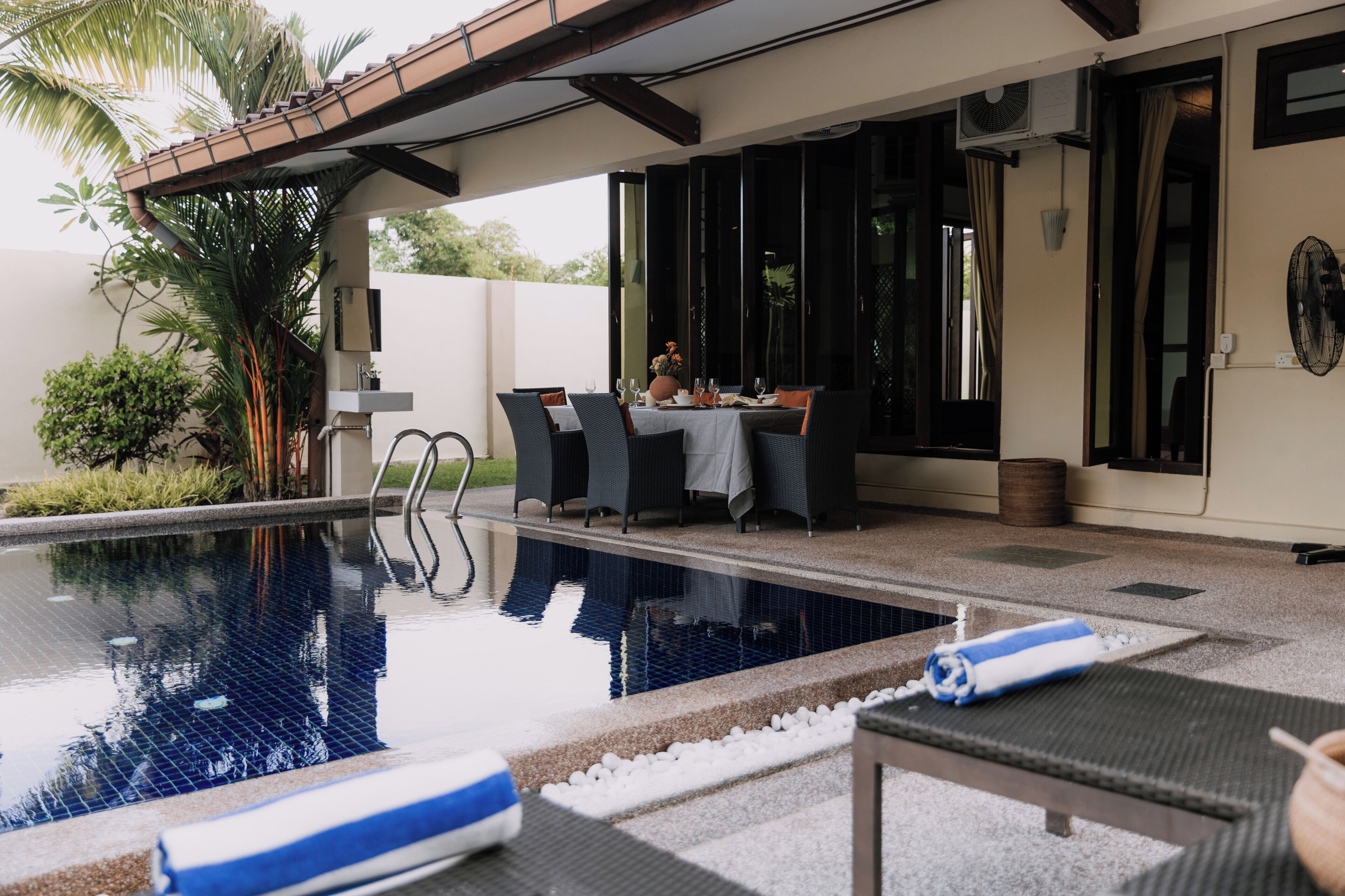 A swimming pool with lounge chairs, a dining area with tables and chairs, and a covered patio with a view of the pool.
