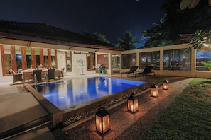 Una piscina con zona de patio, mobiliario exterior y faroles decorativos.