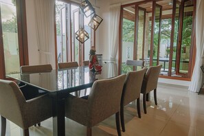 A dining area with a glass table, chairs, and a view of greenery outside. - The Villa - Luxury Private Pool Villa (Langkawi)
