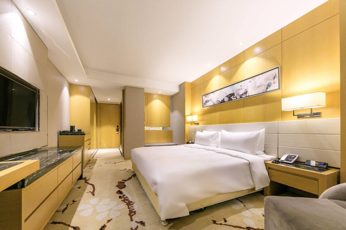 Habitación de hotel con cama, mesita de noche, lámpara y televisión en la pared.