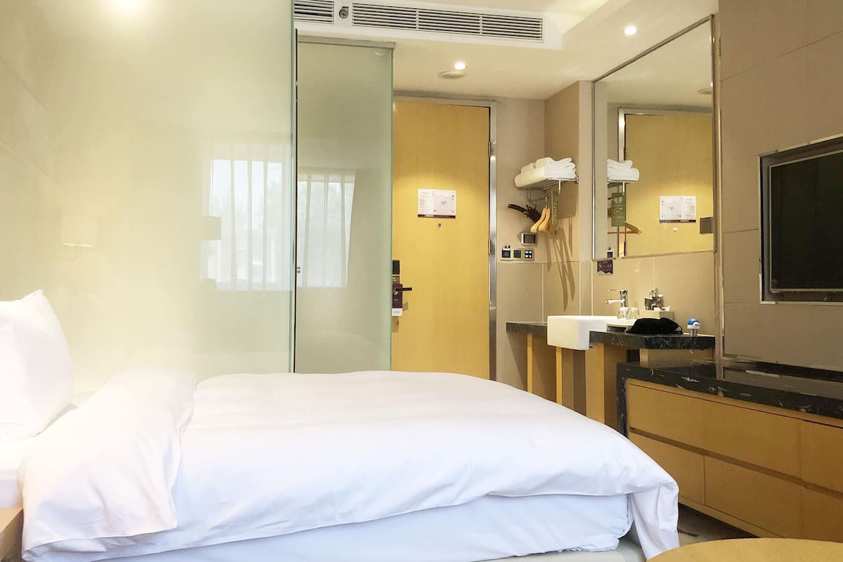 Una habitación de hotel moderna con una cama, un baño con lavamanos y espejo, y un televisor.
