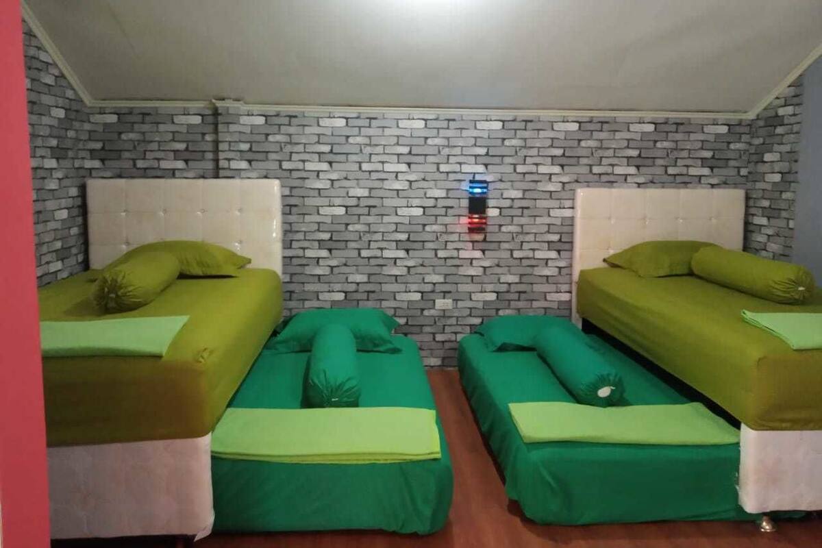 A room with two beds, each with green bedding and pillows, and a brick-patterned wall.
