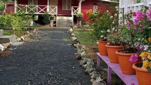 A red house with a porch, surrounded by potted plants and a gravel path.