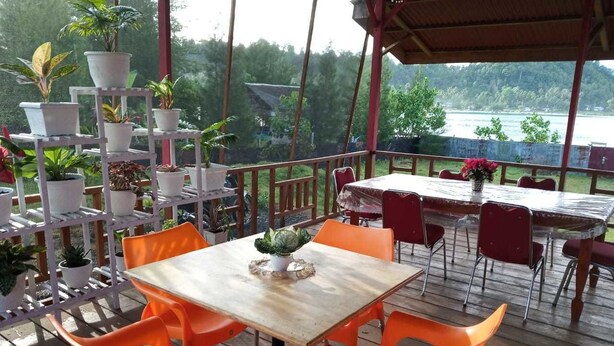 An outdoor patio with a wooden table and orange chairs, surrounded by potted plants and overlooking a body of water.
