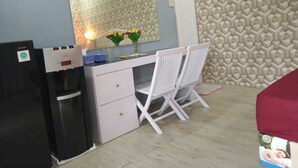 A compact kitchen with a refrigerator, a sink, and a countertop. There is a white chair and a small table with a vase of flowers.