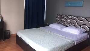 Een net opgemaakt bed met een hoofdbord met patroon, een blauw gordijn en een bord met tekst.