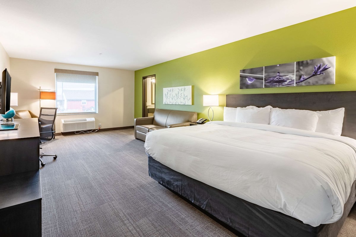 A hotel room with a large bed, a desk with a computer, a chair, and a window.