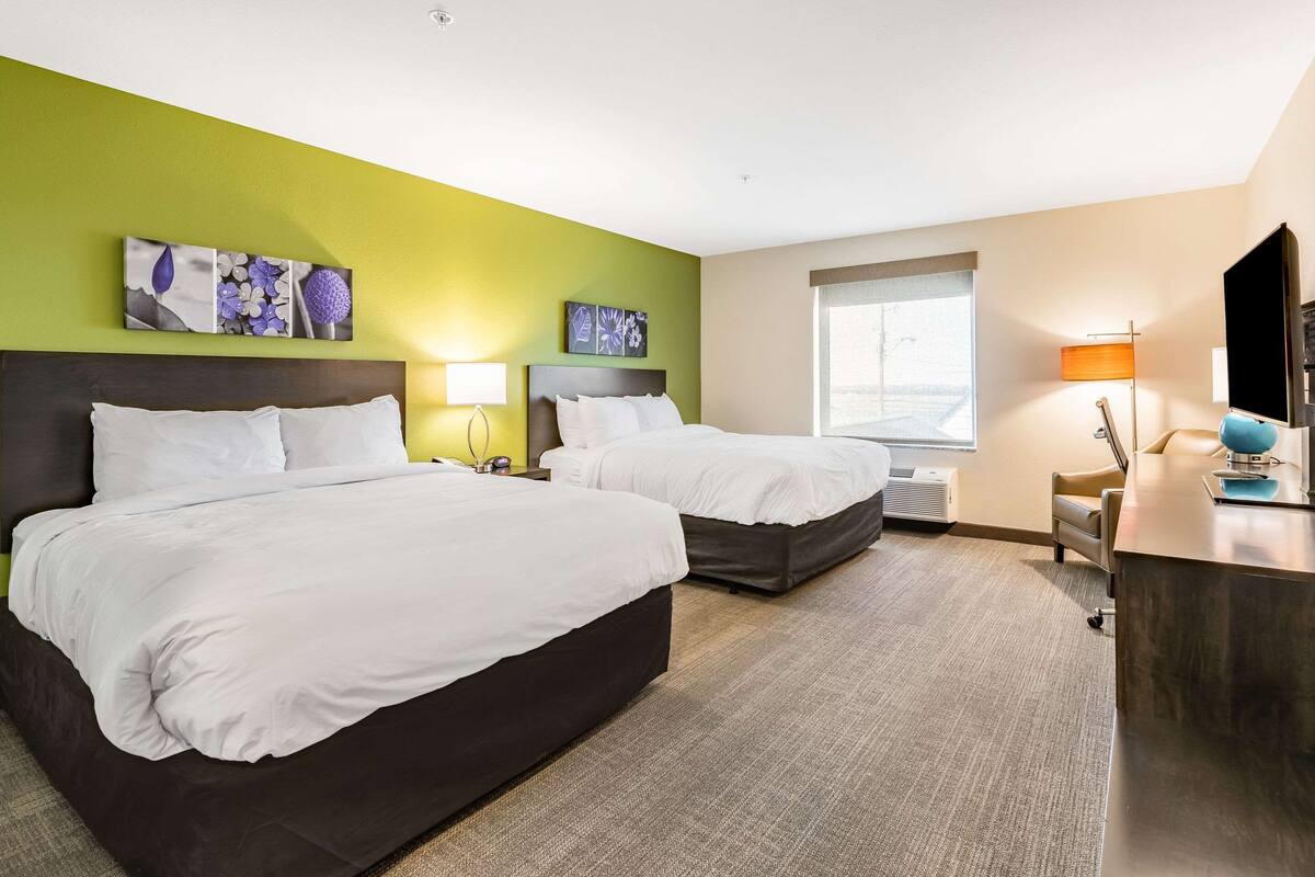 A hotel room with two beds, a desk, a TV, and artwork on the walls.