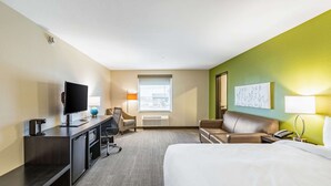 A hotel room with a bed, a desk with a TV, a chair, a couch, a window, and a wall with a painting. - Sleep Inn & Suites Mt. Hope near Auction & Event Center (Mount Hope)