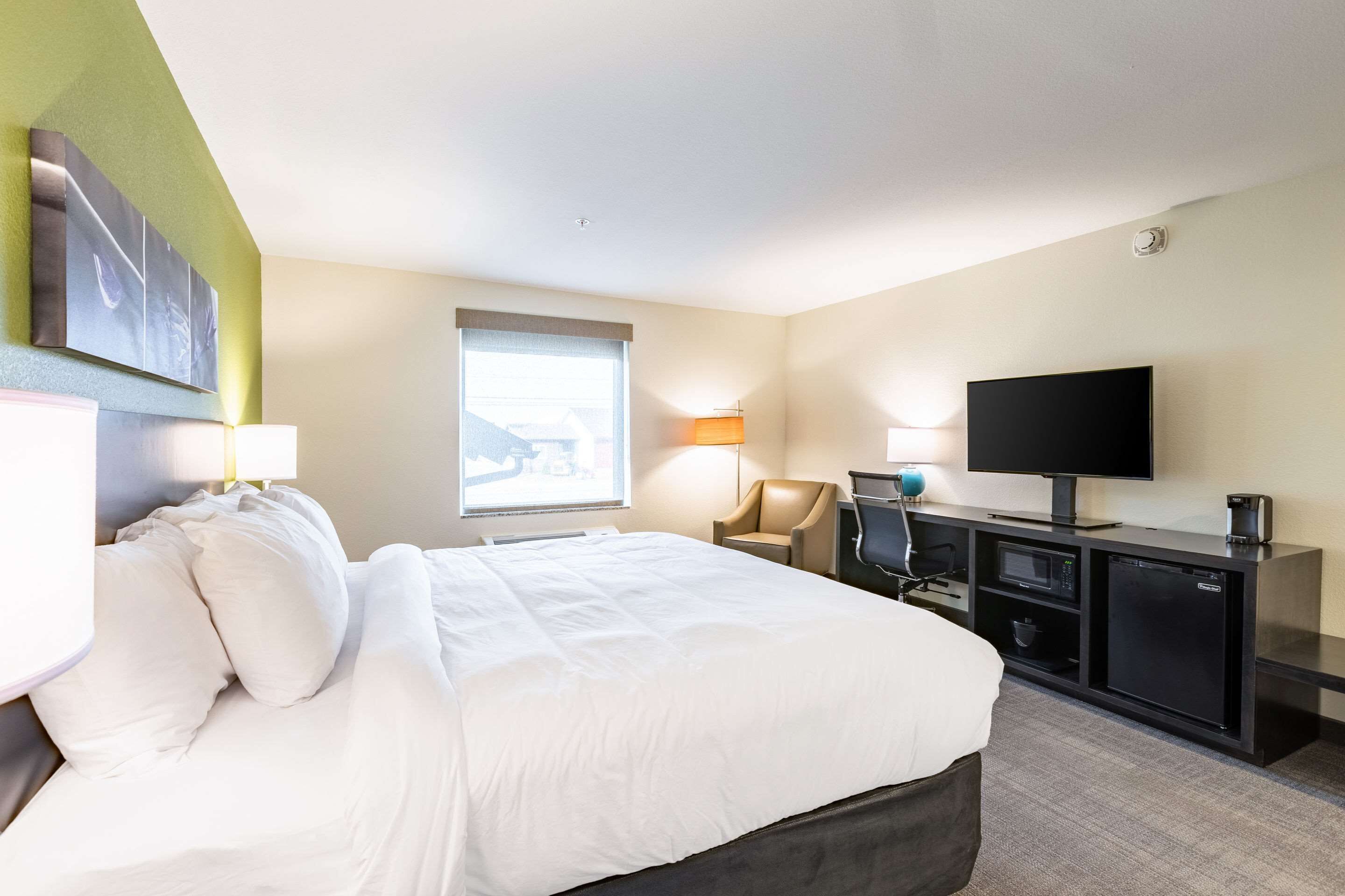 Habitación de hotel con una cama grande, un escritorio con televisor, una silla y una ventana con vistas.