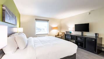 Habitación de hotel con una cama grande, un escritorio con televisor, una silla y una ventana con vistas.