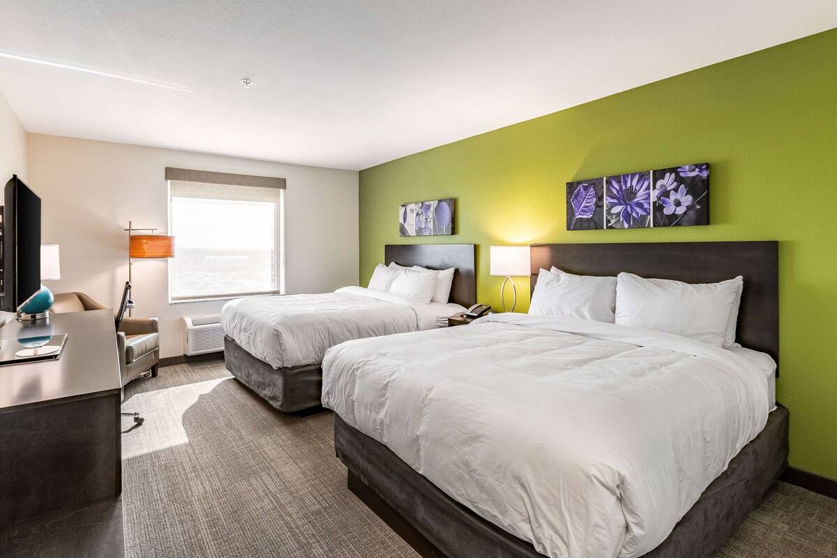 A hotel room with two beds, a desk, a chair, and artwork on the wall.