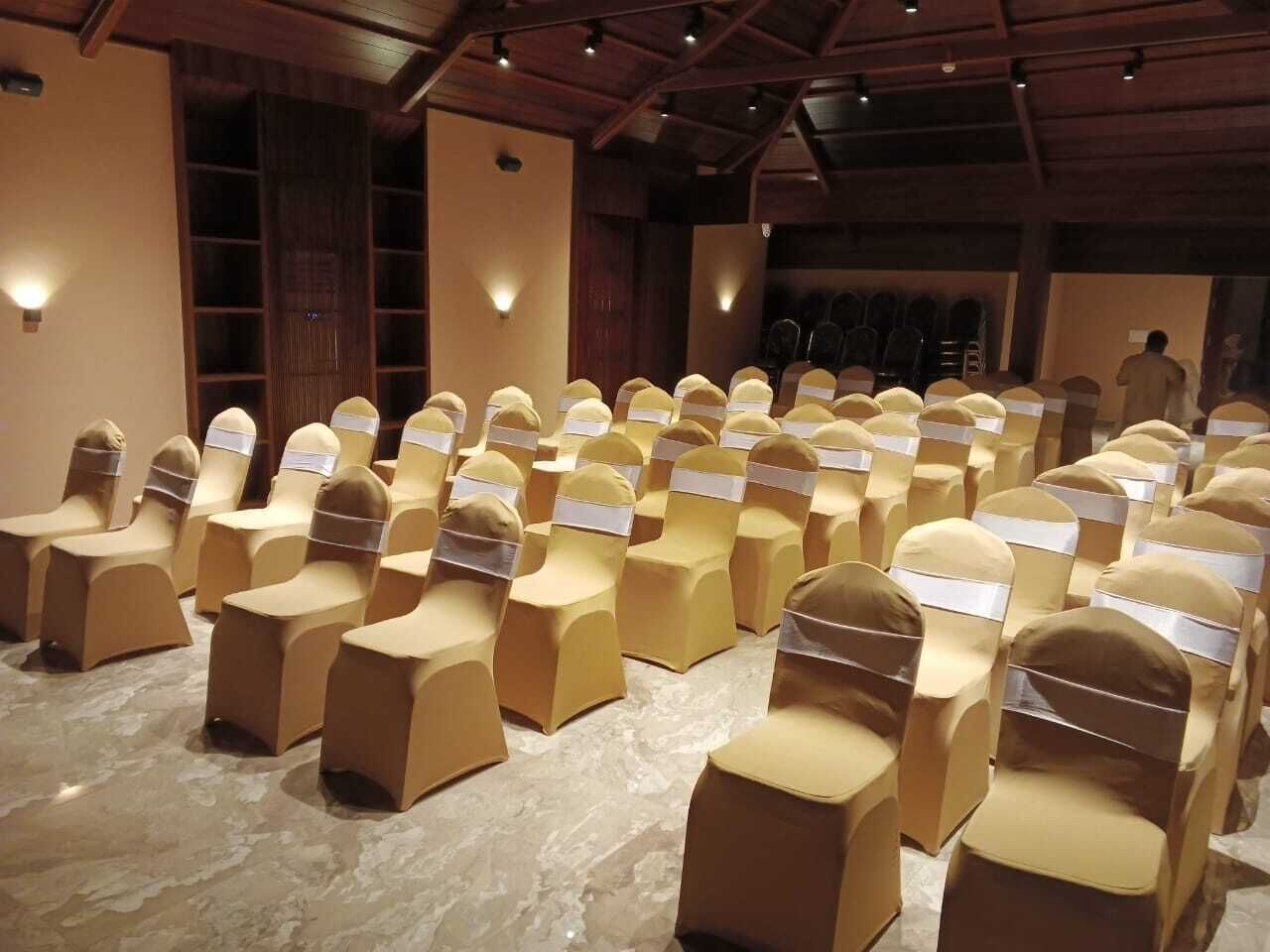Rows of chairs with beige covers and white sashes, arranged in a hall with wooden beams and wall sconces.