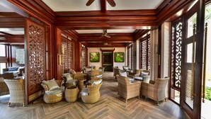 A spacious lobby with herringbone-patterned flooring, wicker furniture, and decorative wooden panels. - Sea Shell Samssara (Port Blair)