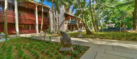 A hotel with a modern architectural design, featuring a courtyard with palm trees and a decorative fish sculpture.