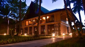 A two-story building with large windows and a balcony, surrounded by palm trees and a well-lit pathway. - Sea Shell Samssara (Port Blair)