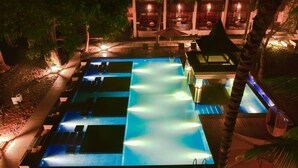 A nighttime view of a hotel swimming pool with multiple lanes, surrounded by palm trees and outdoor seating areas.