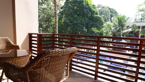 A balcony with wicker furniture, a wooden railing, and a view of a pool and buildings.
