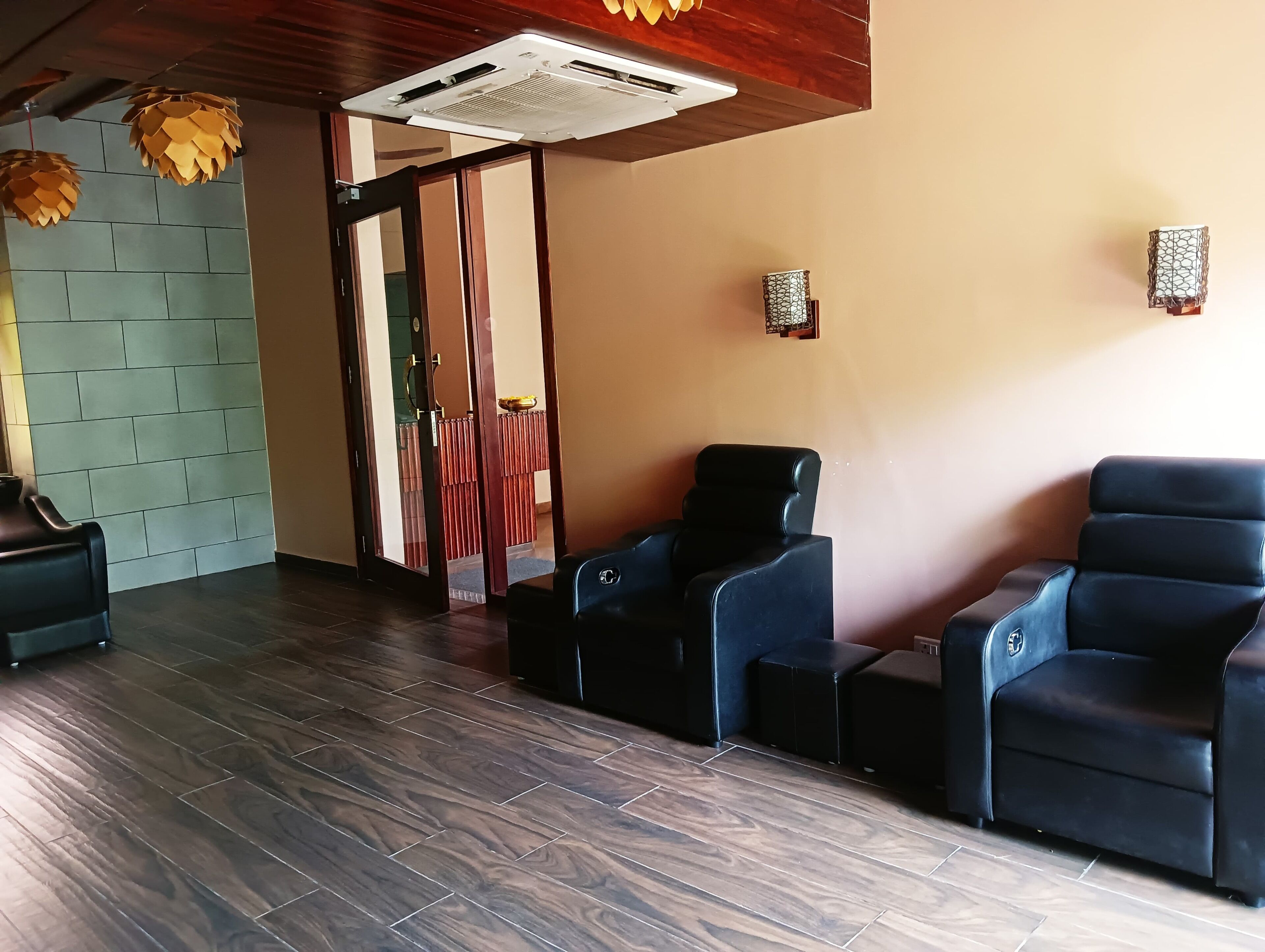 A room with dark wooden flooring, a reception area with a counter and chairs, and a wall with a textured pattern.