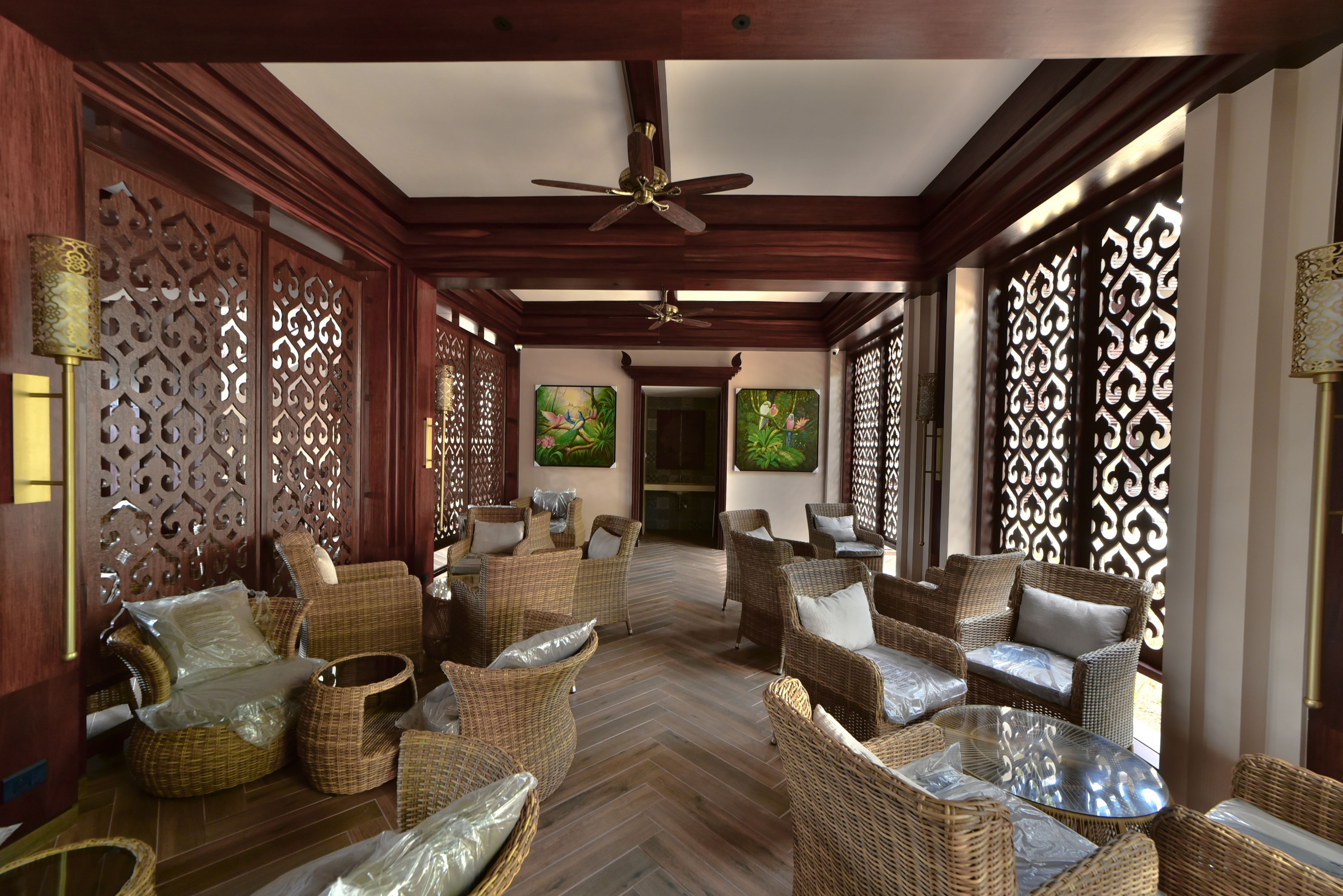 A spacious lounge area with wicker furniture, ceiling fans, and decorative screens.
