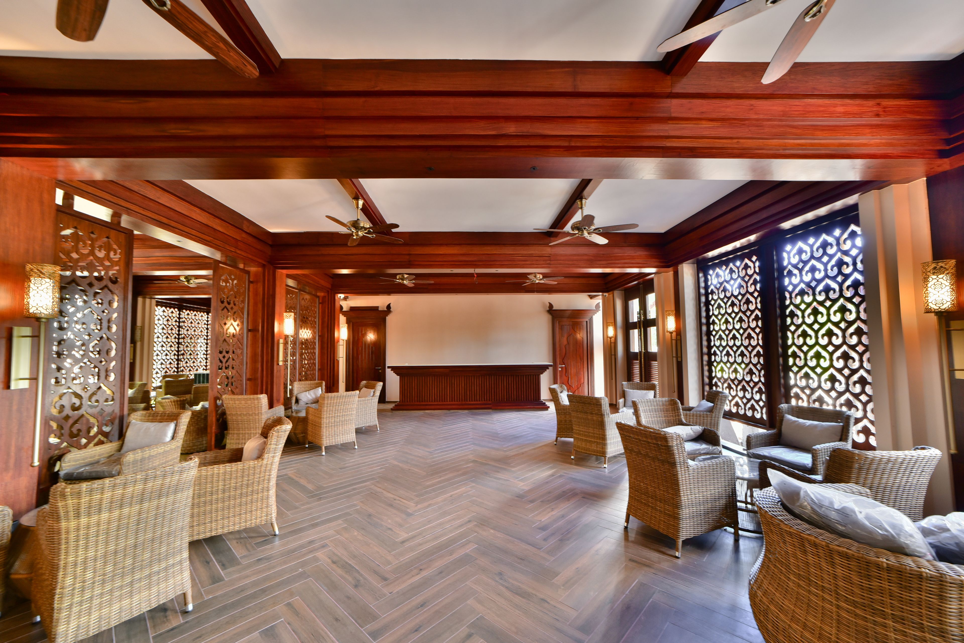 A spacious lobby with wicker furniture, wooden floors, and ceiling fans.